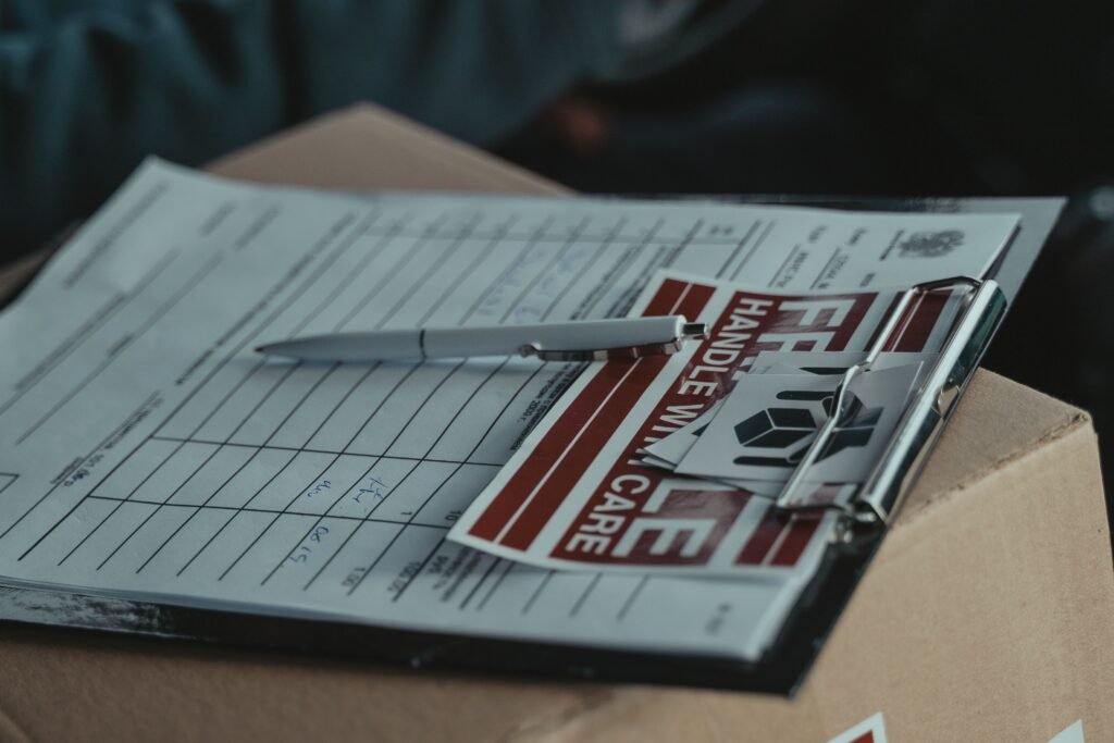 A clipboard with delivery papers and a 'Handle with Care' sticker on a cardboard box.